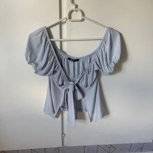 Ljusblå knyt topp från Gina Tricot - Supersöt ljusblå omlottopp från Gina Tricot med puffiga korta ärmar och knyt framtill. Toppen har en bred, djup urringning och är tillverkad i mjuk polyester som känns skön mot huden. Perfekt för dig som gillar romantisk och trendig stil.