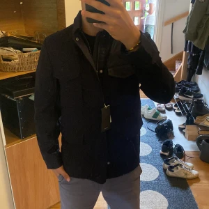 Svart fieldjacka i linne från John Henric - Säljer en svart fieldjacka från John Henric i storlek XS. (Passar S-M) Jackan är tillverkad i linne och har klassisk krage, stora fickor framtill och knappar längs hela framsidan. Perfekt för dig som gillar stilrena och funktionella plagg med snygg passform.