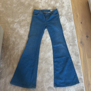 Blå bootcut jeans från Crocker - Säljer ett par blå jeans från Crocker med klassisk bootcut-passform och hög midja. Jeansen har fem fickor, dragkedja och knapp framtill. Materialet är äkta denim och färgen är en snygg mellanblå ton. Perfekt för dig som gillar retrovibbar och breda ben. (Små i storlek så tror de passar en XS samt S