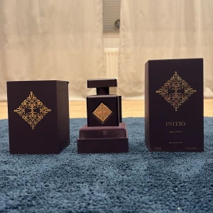 Initio Side Effect Eau de Parfum 90ml - Lyxig parfymflaska från Initio, Side Effect, 90ml. Flaskan är mörklila med fyrkantig form och har en elegant guldfärgad dekor på framsidan. Lock och spraydel är också dekorerade med guld. Kommer i matchande mörklila ask med gulddetaljer. Perfekt för dig som gillar exklusiva dofter.