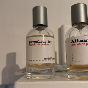 Berzelius 10.0 - oneboldchemist  - Berzelius 10.0 Extrait de Parfum från One Bold Chemist kommer i en stilren, rund glasflaska med metalliskt grått lock. Etiketten är vit med svart och röd text. Parfymen har en ljusgul ton och flaskan har en modern, minimalistisk design.