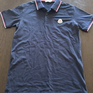 Marinblå Moncler piké t-shirt  - Snygg marinblå piké t-shirt från Moncler används 2-3 gånger pågrund av att den inte passade mig som jag tänkte mig.skriv gärna för frågor och fler bilder!