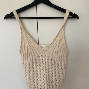 Beige stickad linnetopp från H&M - Säljer en ljusbeige stickad linnetopp från H&M i storlek S. Toppen har ett snyggt virkat mönster och v-ringad hals. Axelbanden är breda och toppen är ärmlös, perfekt för varma dagar. Materialet är mjukt och luftigt stickat.