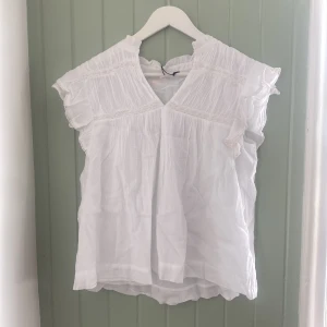 Vit boho blus med spets från Gina Tricot - Supersöt vit boho blus från Gina Tricot med v-ringning, volangdetaljer på axlarna och fina spetsband. Blusen är gjord i tunn bomull och har en luftig, loose passform. Ny med prislap i storlek 170