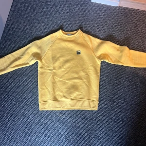 Gul sweatshirt från Mountain Works XS - Säljer en gul sweatshirt från Mountain Works i storlek XS. Tröjan har rund hals, långa ärmar och en liten logga på bröstet. Mjuk insida och klassisk passform, perfekt för dig som gillar enkel och stilren design.