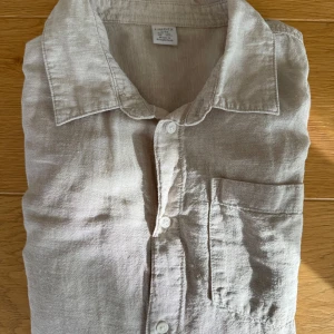Beige linneskjorta  - Snygg beige skjorta från Lindex i luftig linnemix. Klassisk krage, bröstficka och knäppning framtill. Perfekt för en chill och stilren look, passar lika bra över en t-shirt. Skjortan har långa ärmar och en relaxed passform.