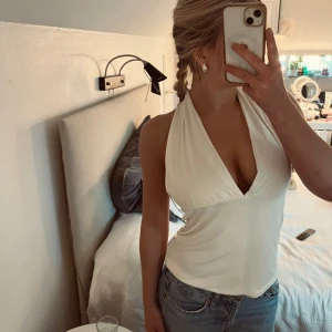 Vit halterneck topp med knyt - Säljer en snygg vit halterneck topp med djup v-ringning och öppen rygg. Köpt från Lager157 och har aldrig använts då jag tyvärr köpt en för stor storlek för mig. Toppen är enkel att matcha och materialet är supermjukt😍