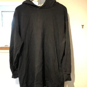 Svart hoodie i ekologisk bomull M/L - Enkel svart hoodie i oversized modell från C, tillverkad i mjuk ekologisk bomull. Tröjan har huva, långa ärmar och breda muddar vid ärmslut och nederkant. Perfekt för en chill och avslappnad stil.