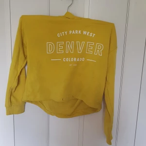 Gul hoodie med Denver-tryck från H&M - Cool gul hoodie från H&M med stort vitt tryck på bröstet där det står 'City Park West Denver Colorado'. Tröjan har huva, långa ärmar och är tillverkad i mjuk bomull. Perfekt för dig som gillar streetstyle och vill sticka ut med färg.