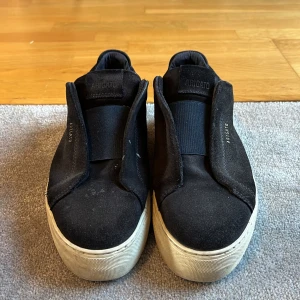 Svarta laceless 360 sneakers från Axel Arigato - Snygga svarta sneakers från Axel Arigato med en stilren design. Skorna har en tjock vit sula och är tillverkade i mocka. Perfekta för en avslappnad stil.. obs dom är sönder inuti. 