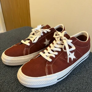 Converse One Star vinröda sneakers mocka - Snygga Converse One Star sneakers i vinröd mocka med vita stjärndetaljer på sidorna och vita snören. Klassisk låg modell med vit sula och diskreta kontrastsömmar. Perfekta för dig som vill ha en retrovibe och sticka ut med färg.