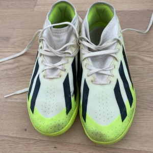 Adidas Crazyfast fotbollsskor gul/vit inomhus med bra skick  - Säljer ett par Adidas Crazyfast fotbollsskor i vitt och neongult med svarta ränder. Skorna har snörning, låg profil och platt sula, perfekt för snabba rörelser på planen. Tillverkade i syntetmaterial och designade för inomhusspel.