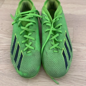 Gröna adidas fotbollsskor med dobbar  - Säljer ett par riktigt snygga gröna adidas fotbollsskor med svarta ränder på sidorna. Skorna har snörning och mönstrad ovandel i syntetmaterial. Utrustade med fasta dobbar för bra grepp på planen. Perfekta för dig som vill sticka ut på matchen!