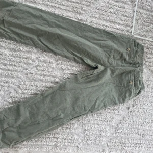 Olivgröna linnebyxor från Zara - Snygga olivgröna linnebyxor från Zara med elastisk midja och knappar bak på fickorna. Byxorna har en avslappnad passform och är perfekta för en chill och stilren look. Materialet är lätt och andas, vilket gör dem sköna att bära under varmare dagar.