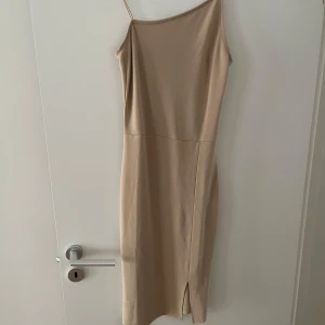 Beige midiklänning - Säljer en stilren beige klänning från NA-KD i storlek M. Klänningen har smala axelband, rak passform och en liten slits framtill. Använd 1 gång, nyskick.