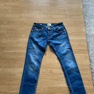 Morris jeans , 32/34 - Säljer ett par klassiska blå jeans med snygga kontrastsömmar och broderad Morris logga på myntfickan. Bakfickorna har coola vågformade sömmar. Jeansen har normal passform och är tillverkade i jeansmaterial. Perfekta för dig som gillar stilrena detaljer.