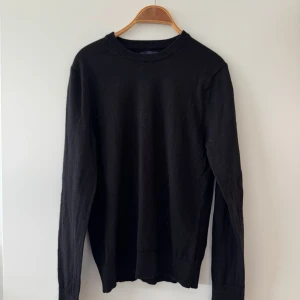 Riley merinoull tröja  - En stilren svart långärmad merinoull tröja med rund halsringning. Tröjan har en klassisk passform och ribbade muddar vid ärmslut och nederkant. Perfekt att matcha med jeans eller kjol för en enkel och snygg look.