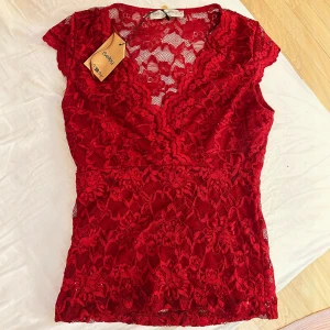 Röd spetsblus med v-ringning Rinascimento - Supersnygg röd blus från Rinascimento i spets med blommigt mönster. V-ringning, extra tyg vid brösten, inte genomskinlig framtill! Köpt på Sellpy, aldrig använd då den var lite för stor för mig som är en XS!♥️