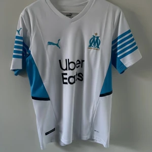 Marseille fotbollströja - Riktigt clean fotbollströja med Marseille som är perfekt nu till sommaren! Luftigt material vilket gör den perfekt under en varm sommardag!Jättefint skick med inga defekter! 
