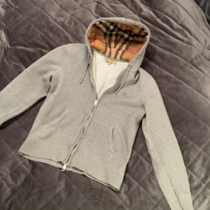 Grå hoodie från Burberry med dragkedja - Säljer en stilren Burberry kofta i grått, använd ytterst få gånger på en semesterresa, ser i princip ny ut. Kommer med kvitto, så inget jävla afghan fejk. Köpte för 3900 kr, står på kvittot. Folk ger alltid komplimanger när man har den på, den sticker ut på rätt sätt u know. Säljer bara för att jag vill testa nåt nytt i garderoben.