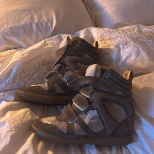 Isabel Marant wedge sneakers grå mocka - Snygga wedge sneakers från Isabel Marant i grå mocka med coola paneler och kardborreband. Skorna har hög siluett, rund tå och platt gummisula. Perfekta för dig som vill ha en sportig men edgy look med extra höjd. Men säljer pga för små på mig som har strl 40❤️
