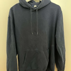 Mörkgrå hoodie med huva och ficka - Enkel och stilren mörkgrå hoodie med huva och snörning. Tröjan har en stor magficka och långa ärmar, perfekt för en avslappnad look. Tillverkad i mjuk bomull som känns skön mot huden.