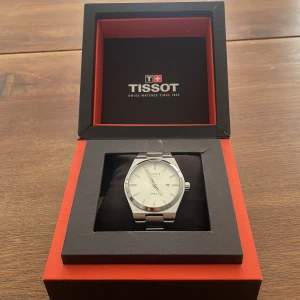 Tissot PRX silverfärgad klocka - Snygg Tissot PRX klocka i stilren design med silverfärgat armband och boett i rostfritt stål. Urtavlan är vit med minimalistiska index och diskret logga. Länken är robust och har Tissot ingraverat på spännet. Perfekt accessoar för dig som gillar klassisk stil.