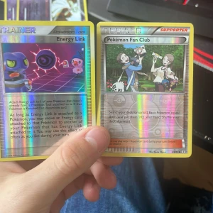 Pokémon Trainer Cards: Energy Link & Pokémon Fan Club - Två glittriga Pokémon Trainer-kort: Energy Link och Pokémon Fan Club. Perfekta för samlare och spelare som vill boosta sitt deck med snygga och användbara kort. Passar dig som älskar Pokémon och vill sticka ut i spelet!