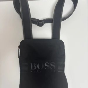 Hugo boss axelväska  - Väskan säljs inte längre och är köpt för ungefär 2-3 år sen och har bara kommit till användning max 3/4 gånger så den har bara stått i garderoben utan någon nytta. Helt felfri utan några skador. Annars passar den alla olika längder där man kan lösa det genom väskans bak sida. Köpt för 1349kr