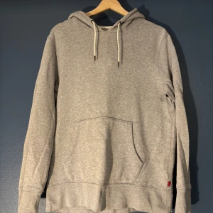 Levi's Grå Hoodie - En stilren grå hoodie från Levi's i storlek S. Tröjan har huva med snörning, känguruficka framtill och klassisk röd Levi's-tag vid sidan. Tillverkad i mjuk bomullsmix och har långa ärmar. Perfekt för chill dagar eller när du vill ha en enkel look.