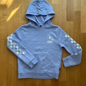 Ljuslila hoodie från Vans med blommor - Säljer en ljuslila hoodie från Vans i storlek medium. Tröjan har blommigt tryck på bröstet och schackrutiga detaljer med små blommor längs ärmarna. Klassisk känguruficka och huva. Perfekt för dig som gillar streetwear och coola detaljer.