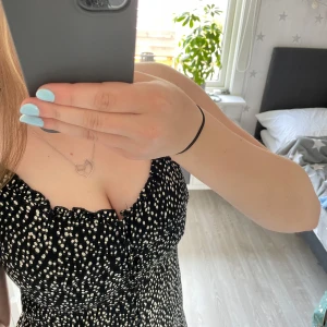 Supersöt sommarklänning  - Supersöt svart klänning med vita prickar och knappar framtill. Klänningen har en liten slits, figurnära passform och är ärmlös. Materialet känns mjukt och svalt, perfekt för varmare dagar. Snygg volangkant upptill ger en extra touch. Står ingen storlek men jag skulle gissa på XS/S. Jättefint skick 