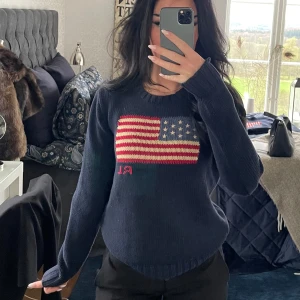 Mörkblå stickad tröja Polo Ralph Lauren iconic flag - Mörkblå stickad tröja från Polo Ralph Lauren med amerikansk flagga och RL-broderi framtill. Tröjan har rund halsringning, ribbade muddar och lång ärm. Nypris ca 4500kr