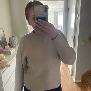 Beige stickad tröja med hög krage - En stilren beige stickad tröja med hög ribbad krage och långa ärmar. Tröjan har en loose passform och är perfekt för lager-på-lager. Enkel och clean design utan mönster eller detaljer, passar till allt och är supermjuk.