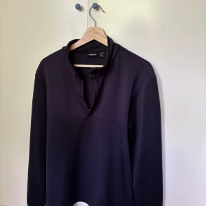 Svart half zip tröja från Crivit - Svart långärmad tröja från Crivit med half zip-dragkedja och hög krage. Tillverkad i mjukt syntetmaterial, perfekt för träning eller chill. Enkel och stilren design utan mönster eller extra detaljer. Passar dig som gillar sportig och clean look.