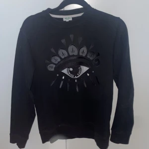 Svart Kenzo tröja - Svart tröja från Kenzo i storlek XS med ikoniskt broderat ögonmotiv på bröstet. Tröjan har rund halsringning, långa ärmar och är gjord i mjuk bomull. Perfekt för dig som gillar streetstyle och vill sticka ut med en cool detalj.