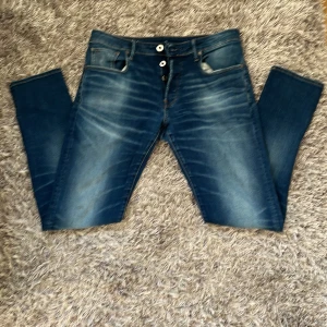 G-Star RAW 3301 Slim jeans blå - Snygga blå jeans från G-Star RAW, modell 3301 Slim. Klassisk femficksdesign med slitningar och ljusare partier framtill. Jeansen har bruna kontrastsömmar, logga på bakfickan och läderpatch i midjan. Perfekt passform med smal siluett.