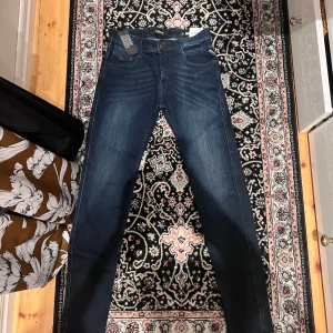 Replay Anbass slim jeans blå 29/32 - Snygga mörkblå Replay Anbass jeans med slim fit och power stretch. Klassisk femficksmodell med dragkedjegylf och Replay-logga på fickan. Jeansen har en lätt tvättad look och sitter riktigt schysst på kroppen.