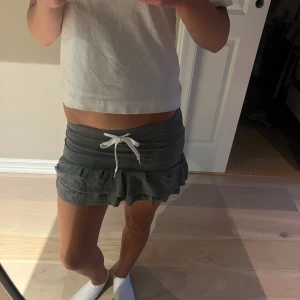 Mörkgrå volangkjol med snörning - Supersöt mörkgrå kortkjol med volangkant och vit snörning i midjan. Kjolen har en tight passform upptill och är gjord i mjukt bomullsmaterial, perfekt för en chill look. Materialet är väldigt stretchigt och passar därför allt ifrån S till xxs. Har sytt själv så därav priset!  