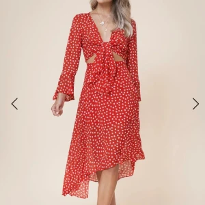 Röd blommig omlottklänning med knyt - Superfin röd klänning med vita blommor, v-ringning och knyt framtill. Klänningen har långa ärmar med volangkant, cut-outs vid midjan och asymmetrisk nederkant. Perfekt för sommarens alla tillfällen!