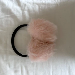 Rosa fluffiga öronvärmare - Supermjuka öronvärmare med fluffig rosa päls och svart båge. Perfekt accessoar för att hålla värmen och ge en söt touch till din vinterstil.