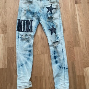 Amiri jeans - äkta - Unika ljusblå jeans från Amiri med tie dye-effekt, stora svarta stjärnapplikationer och slitna detaljer. Byxorna har broderad AMIRI-logga på låret och flera coola hål och rivna partier. Tillverkade i 100% bomull för skön känsla.