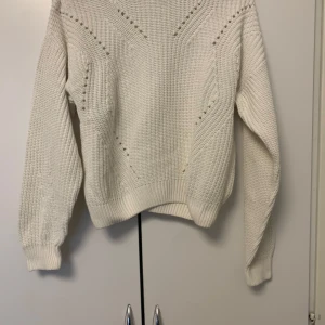 Vit stickad tröja med hålmönster - Säljer en vit stickad tröja med snygga håldetaljer och strukturstickning. Tröjan har långärmad passform och ribbade muddar vid ärmslut och nederkant. Perfekt för lager på lager under kyliga dagar.