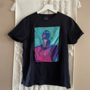 Svart Limitato t-shirt med konstmotiv - Svart t-shirt från Limitato i mjuk bomull med ett stort färgstarkt konstmotiv på bröstet i blått, turkost och rosa. Klassisk passform med rund hals och korta ärmar. Limitato-logga diskret på ryggen. Perfekt för dig som gillar unika prints.