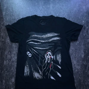 Svart t-shirt med Scream-motiv - Cool svart t-shirt med tryck inspirerat av Edvard Munchs Skriet och Scream-masken. Motiv i vitt, rött och grått som ger en unik och edgy vibe. Perfekt för dig som gillar skräck eller vill sticka ut med din stil. Klassisk passform och rund hals.