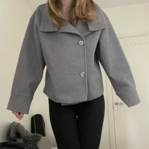 Grå kappa från Gina Tricot XS - Säljer en snygg grå kappa från Gina Tricot i kortare modell. Kappan är knapp använd. Perfekt för hösten när det blir lite kallare  och för dig som gillar en clean stil. Passar snyggt till både jeans och kjol.