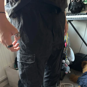 Svarta cargopants med fickor - Säljer ett par svarta cargopants med flera praktiska fickor på sidorna och bak. Byxorna har elastisk midja för extra komfort och är tillverkade i ett mjukt bomullstyg. Perfekta för en avslappnad och cool streetstil. Säljs då de blivit för små:)