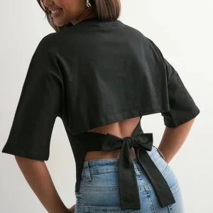 Svart topp med knyt i ryggen - Svart croppad topp med halvlånga ärmar och öppen rygg som knyts med en bred rosett baktill. Toppen har en tight passform runt midjan och är tillverkad i mjuk bomull. Perfekt för dig som gillar trendiga detaljer och vill sticka ut lite extra. Den är lite lite nopprig på insidan men inget man ser när man har på sig den. Finns även två svaga vita sträck på insidan av tröjan (tror de är från en deo). Men inget men heller ser när man har på sig den. Skriv vid frågor❤️