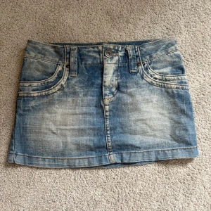 Blå jeanskjol från Only - Snygg blå jeanskjol från Only med slitna detaljer och klassiska fickor fram och bak. Kjolen har bälteshällor, knapp och dragkedja framtill samt dekorativa sömmar på bakfickorna. Perfekt för dig som gillar en cool och avslappnad stil.