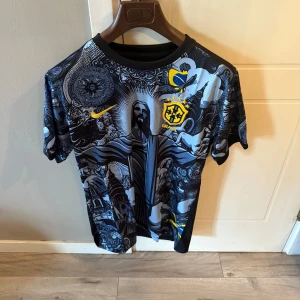 Nike Brasil grafisk fotbollströja - Snygg Brasilien fotbollströja från Nike med unikt grafiskt tryck i svart, grått och blått på framsidan. Gult broderat Nike-märke och Brasilien-emblem. Baksidan är helsvart med litet emblem upptill. Tillverkad i lätt och ventilerande material.